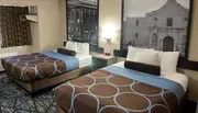 The image shows a hotel room with two neatly made double beds featuring brown and blue bedding, modern decor, and black-and-white wall art depicting historical scenes.