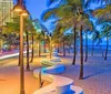 The image captures a vibrant and colorful evening scene of a palm-lined beachside promenade with light trails from moving vehicles characteristic street lamps and modern buildings in the background