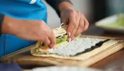 A person is preparing sushi by rolling ingredients in seaweed on a bamboo mat.