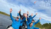 A group of happy people wearing blue shirts are raising their hands in the air while seated on a boat.