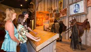 Three visitors are engaging with an interactive exhibit at a museum focused on conservation and hunting.