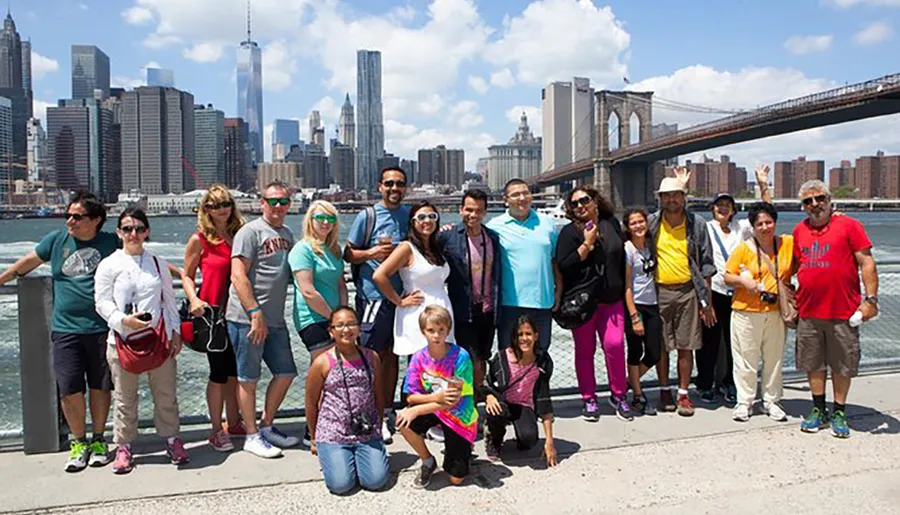 A diverse group of people poses for a photo with the Brooklyn Bridge and the Manhattan skyline in the background.