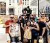 A group of people is posing for a photo in front of a dark statue of Batman at Rockefeller Center with the iconic golden Prometheus statue and international flags in the background