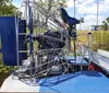The image shows a close-up view of an airboat, with its large cage-like fan structure and seating area, parked by a water body on a sunny day.