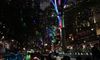 People on a boat ride admire a tree adorned with colorful lights, creating a festive atmosphere along a riverside.