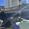 A group of people on a boat are passing under a bridge marked 