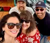 A group of four people is smiling together on a boat, with a waterfront view in the background.