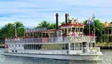 The image depicts a group of passengers enjoying a sightseeing tour on a paddlewheel boat named Carrie B.