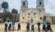 A group of people on electric bikes are posing for a photo in front of an old church with two bell towers.
