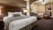 The image shows a neatly arranged hotel room with a king-sized bed, a sitting area, and a whirlpool tub, featuring a contemporary design with warm tones.