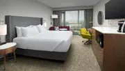 This image shows a modern and neatly organized hotel room with a large bed, a sitting area with a couch and armchair, a work desk, and a television set over a cabinet.