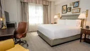 The image shows a neatly arranged hotel room with a large bed, desk, chair, and wall decorations, reflecting a comfortable and tidy guest accommodation.
