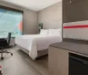 The image depicts a modern and neatly arranged hotel room with two beds a large window offering an outdoor view a desk with a chair and contemporary wall-mounted lamps