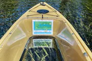 A yellow kayak with a transparent bottom and a map attached to the front is on clear water revealing aquatic plants below.