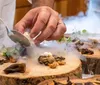 A chef is meticulously plating a dish with tweezers amid a smoky presentation on wooden surfaces suggestive of an upscale gourmet experience