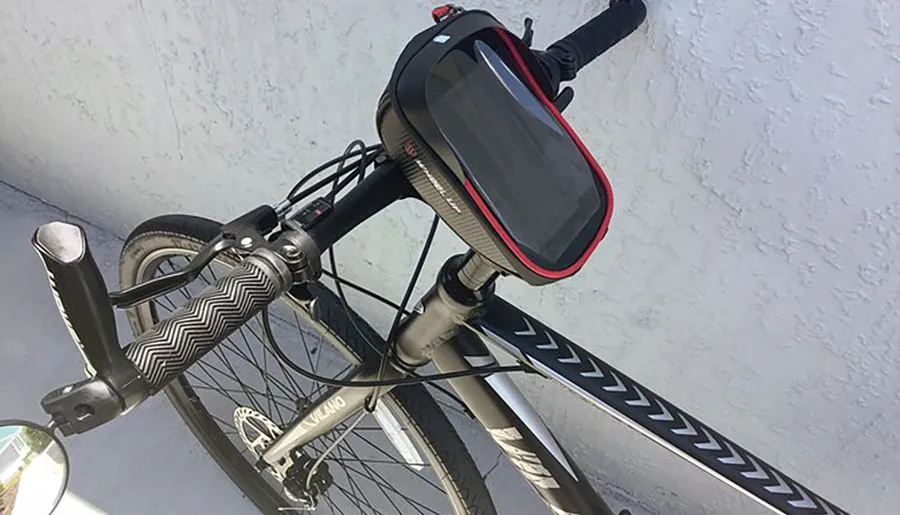 A bicycle is propped against a white wall with a smartphone mounted on its handlebars, possibly for navigation or tracking purposes.