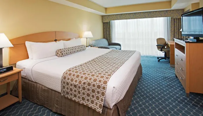 The image shows a neatly arranged hotel room with two beds a desk a TV and a closed curtain