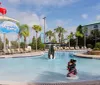 A child-friendly hotel pool area features a Splash Zone with penguin-themed decorations and a view of roller coasters in the distance