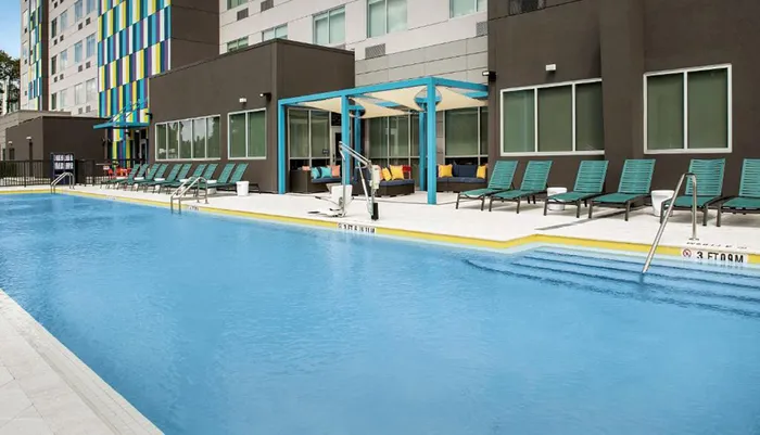A modern outdoor swimming pool with lounge chairs and a colorful building facade in the background