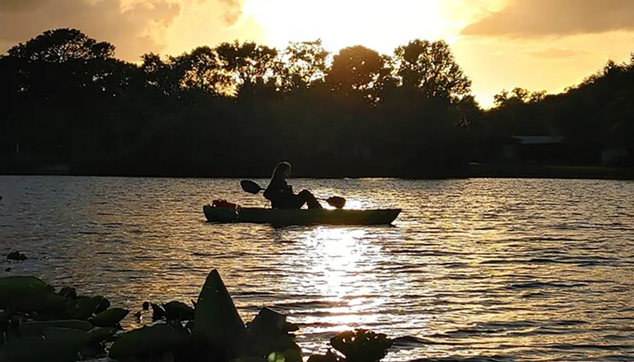 A person is kayaking on a tranquil lake against the backdrop of a sunset.