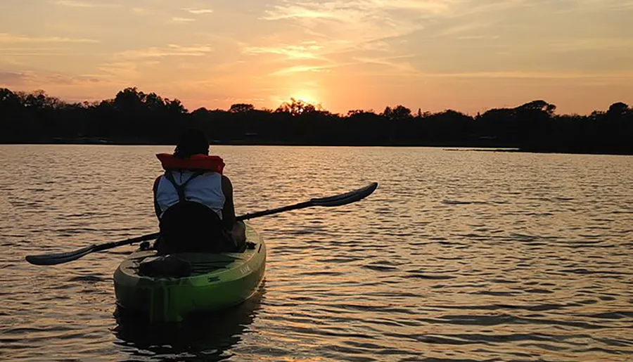 A person kayaks on calm waters against the backdrop of a beautiful sunset.