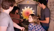 Four people are engaging in an escape room puzzle, working together to solve a challenge involving a circular sun-shaped artifact with puzzle pieces.
