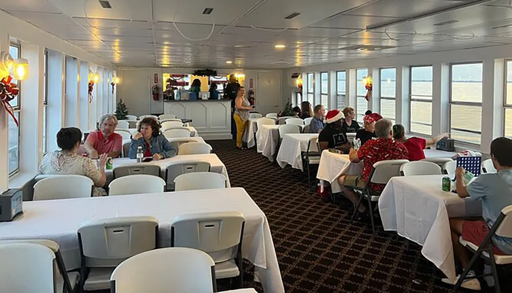 People are casually seated at tables in a ferry or cruise ship dining area decorated with Christmas ornaments suggesting a holiday-themed event or cruise