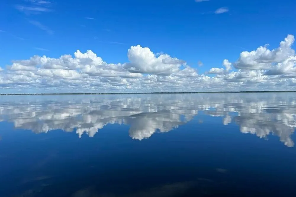 The image features a calm body of water with a clear sky above where the white fluffy clouds are perfectly reflected on the waters mirror-like surface creating a serene and symmetrical natural scene