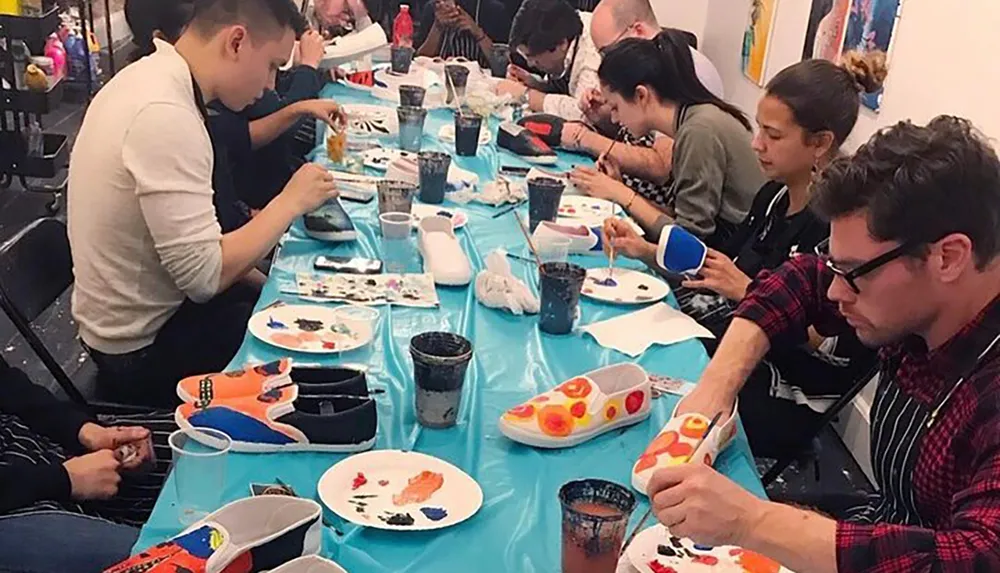 A group of people are focused on hand-painting shoes at a crafting workshop