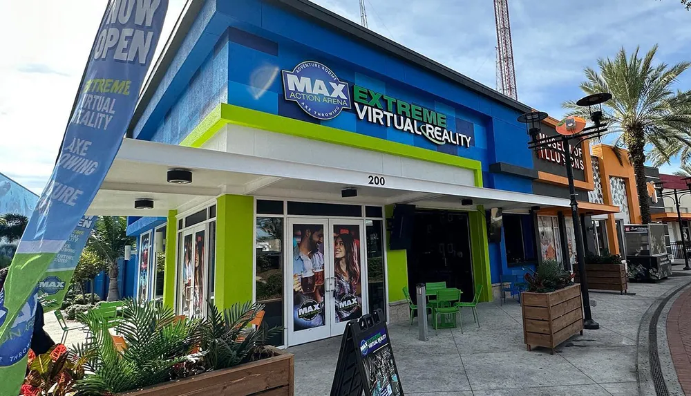 The image shows a vibrant and colorful facade of the MAX Extreme Virtual Reality entertainment venue with a banner that reads NOW OPEN and other attractions nearby