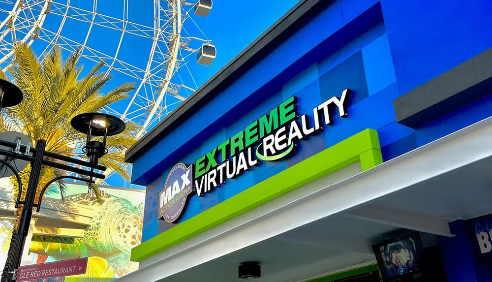 The image shows the bright blue facade of an Extreme Virtual Reality entertainment venue against a clear sky with a large Ferris wheel and palm trees in the background