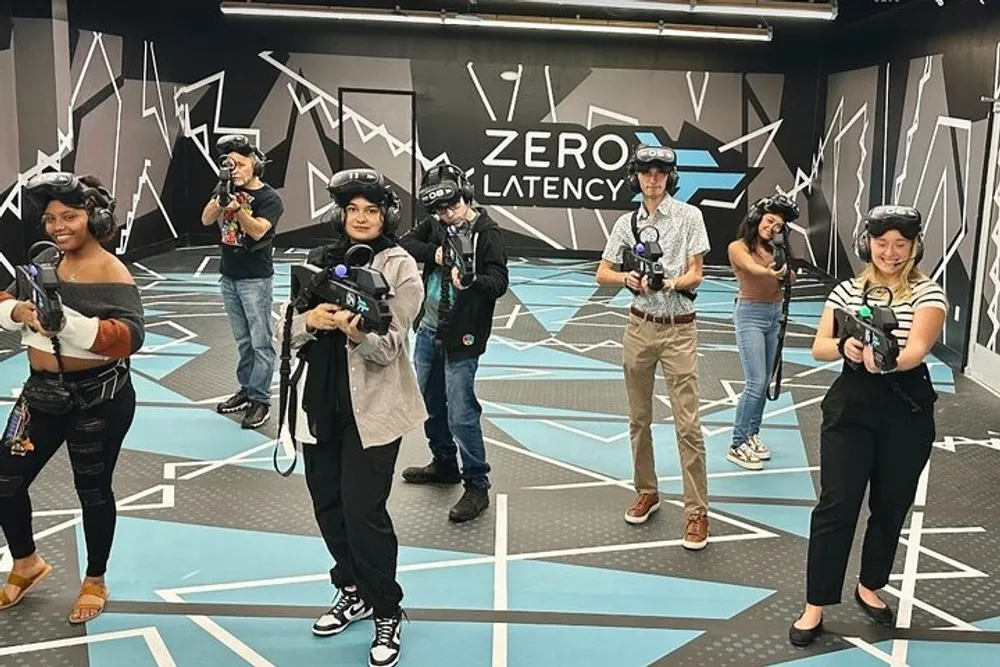 A group of people equipped with virtual reality headsets and gear are ready for an immersive VR experience in a facility with vibrant graphics on the walls and floor