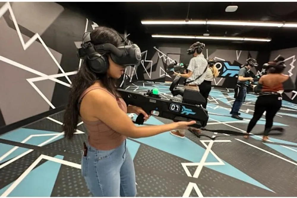Several people are engaged in a virtual reality gaming experience in a room with geometric patterns on the walls and floor