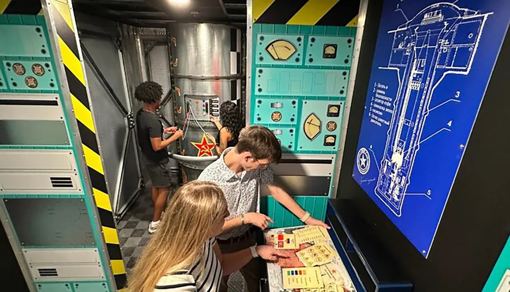 Young individuals are engaged in an activity within a room styled to resemble a spacecraft interior with one examining a blueprint and another interacting with a control panel