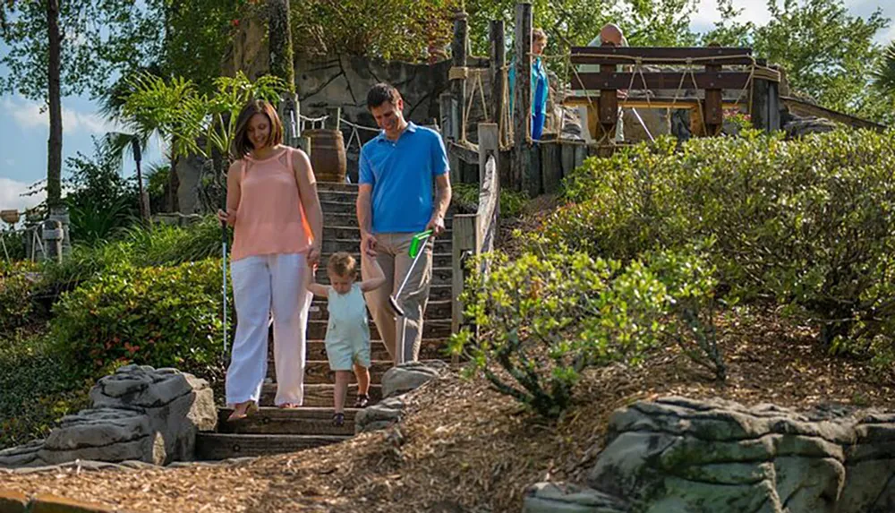 A family is enjoying a sunny day outdoors with two adults guiding a small child down some wooden steps in a lush garden setting