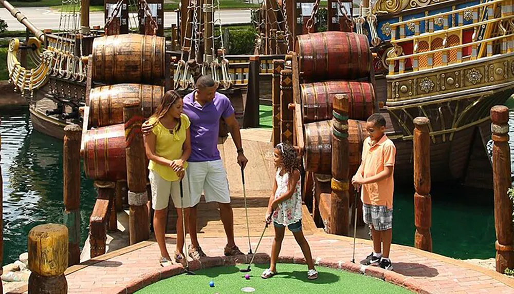 A family of four is enjoying a game of miniature golf with a pirate ship backdrop