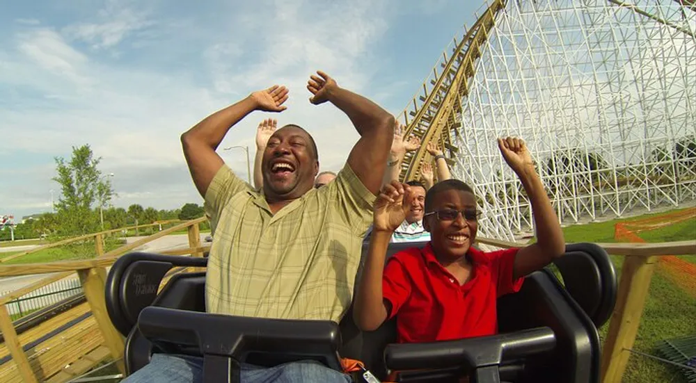 Two people are enjoying a thrilling roller coaster ride their hands raised in excitement with joyful expressions