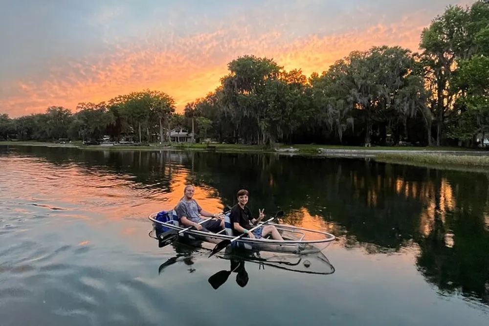 Two people are enjoying a canoe ride on a serene river against a vibrant sunset sky