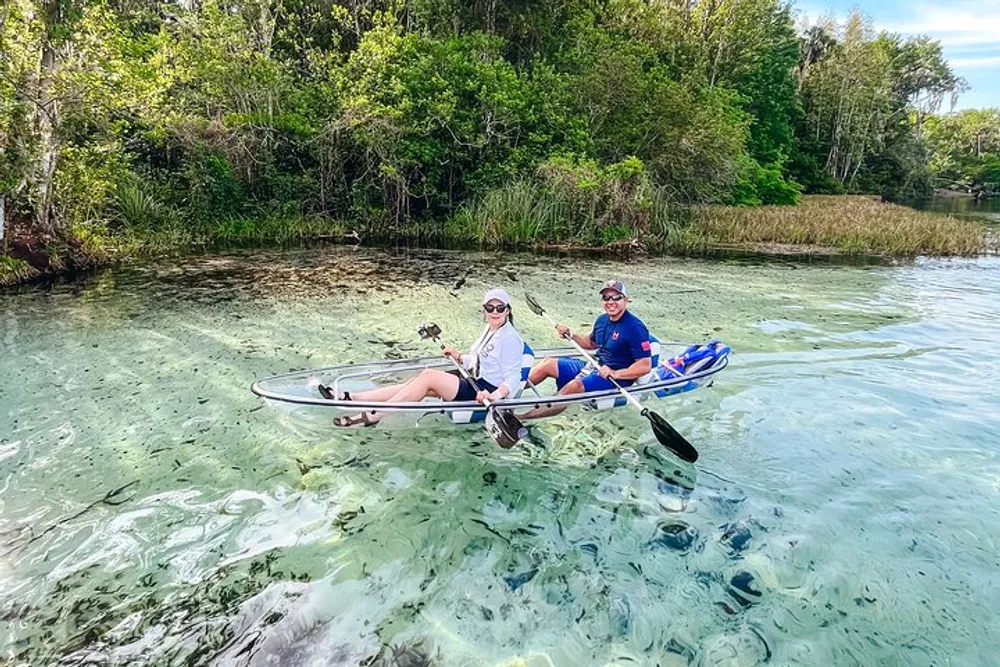Two people are enjoying a sunny day on a clear-water river in a transparent kayak