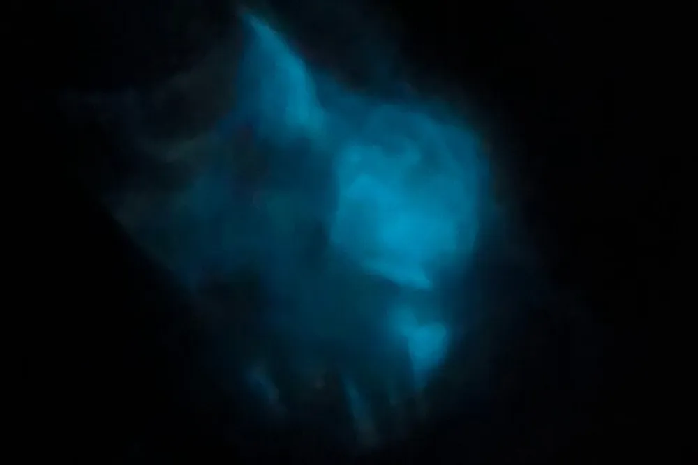 The image shows a blurry blue nebulous form against a dark background resembling a celestial body or a gas cloud in space