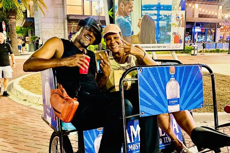 Two individuals are posing with peace signs, smiling for the camera while sitting in a pedicab at night in an urban area.