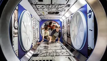 Three people are crawling through a tunnel-like structure designed to resemble the interior of a futuristic spacecraft.