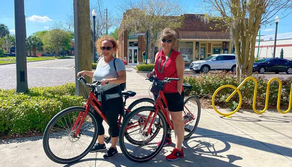 Two people posing with their bicycles on a sunny day in an urban setting