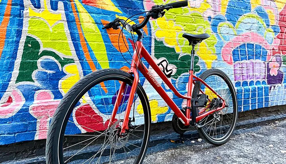 A red bicycle is parked against a vibrant graffiti-covered wall