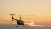 A helicopter flies against a backdrop of a golden sunset sky.