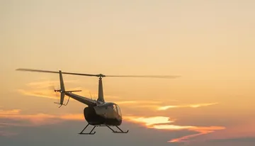 A helicopter flies against a backdrop of a golden sunset sky.