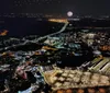 The image shows a nighttime aerial view of a vibrant illuminated cityscape with a bridge crossing a body of water and fireworks bursting in the distance