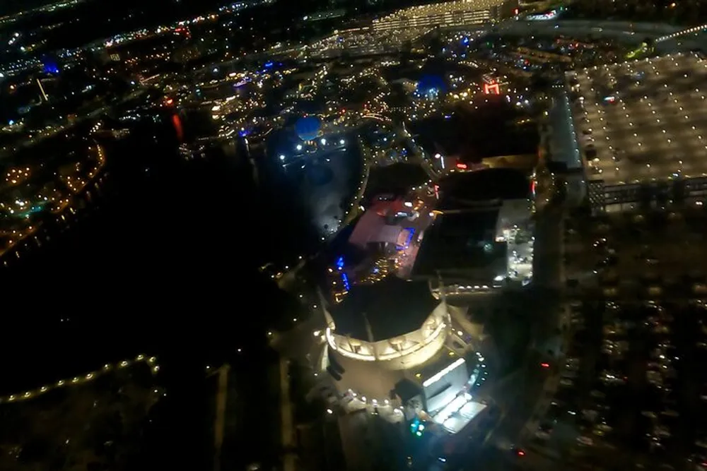 The image shows a nighttime aerial view of a brightly lit urban area with various buildings and streets