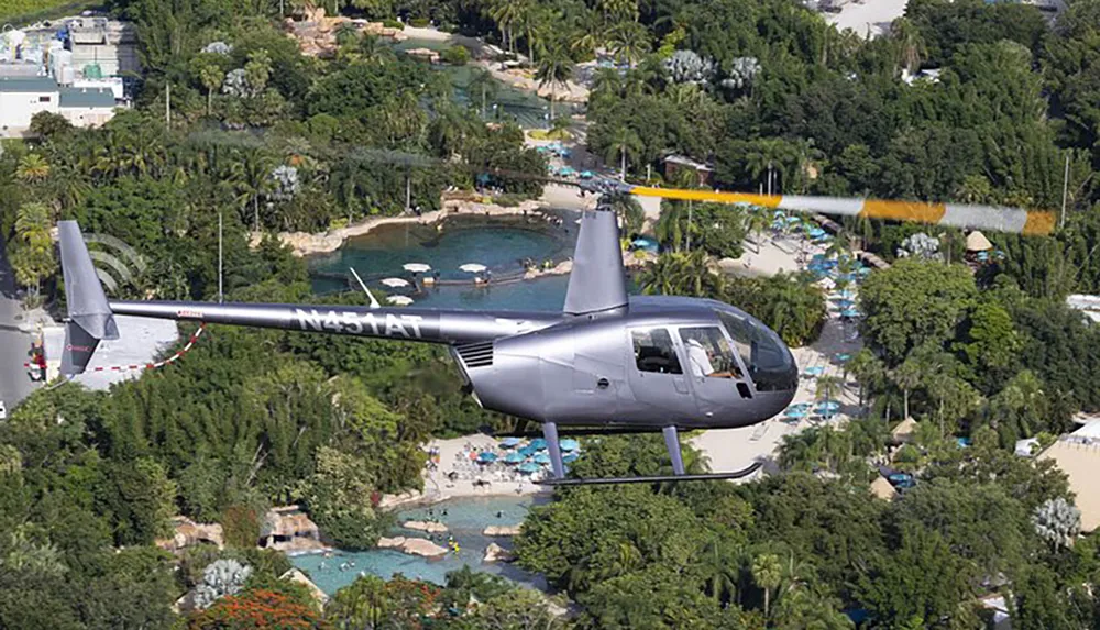 A helicopter is flying over a tropical resort area with pools and lush greenery