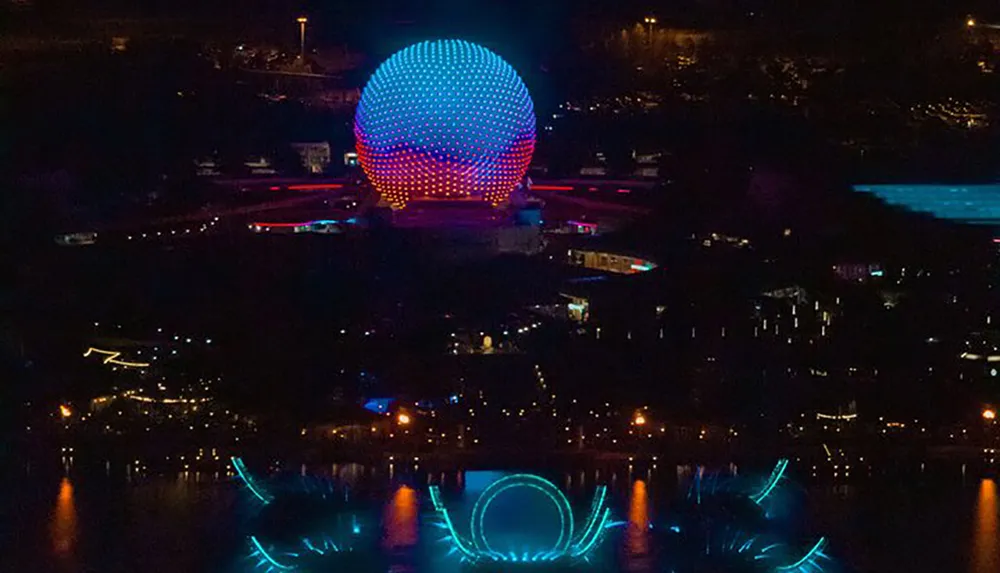 The image shows a striking night view of a brightly lit spherical structure reflecting over water creating a mesmerizing mirror image